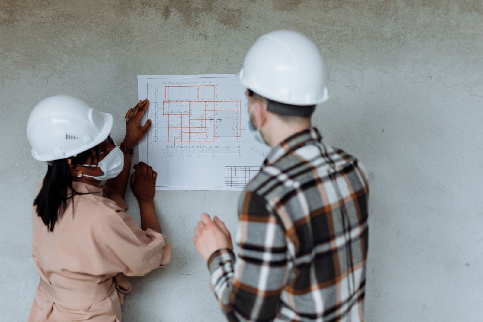 Two people reviewing a construction blueprint pinned to a wall